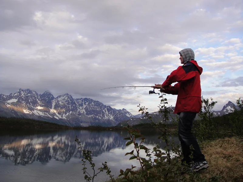 Renate fisker ved et fjellvann med storslått landskap i bakgrunnen